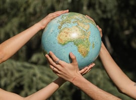 Two pairs of hands holding onto a model of the Earth